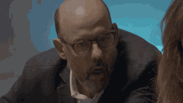 a bald man with glasses looks at a woman