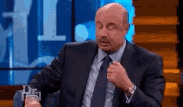a bald man in a suit and tie is sitting in front of a sign that says dr. phil .