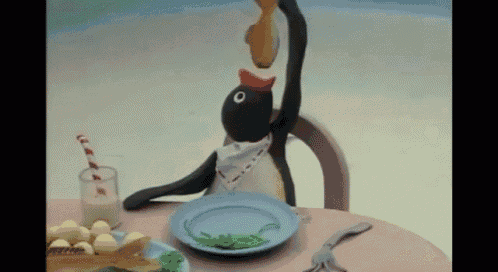 a stuffed penguin is sitting at a table with a plate of food