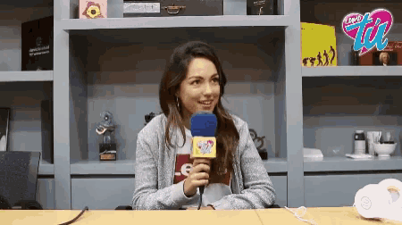 a woman sitting at a table with a microphone in front of a shelf with a sign that says ' radio zoo '