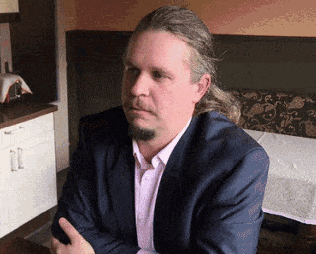 a man with long hair and a ponytail is wearing a blue suit and pink shirt