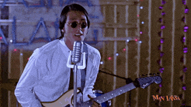 a man is singing into a microphone while holding a guitar in front of a wall that says man laksa