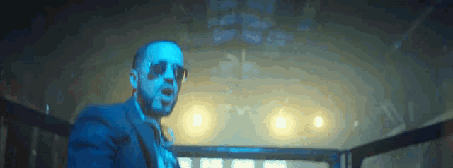 a man in a blue suit and sunglasses stands in a dark room