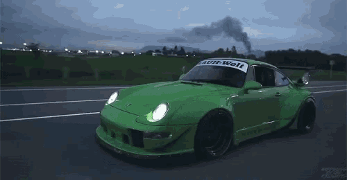 a green porsche is driving down a road with smoke coming out of the exhaust pipe .