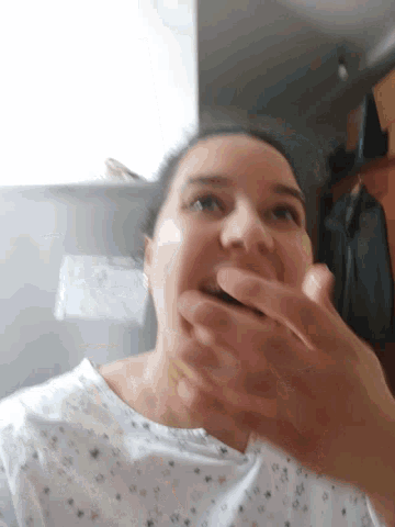 a woman covering her mouth with her hand while wearing a white shirt with stars