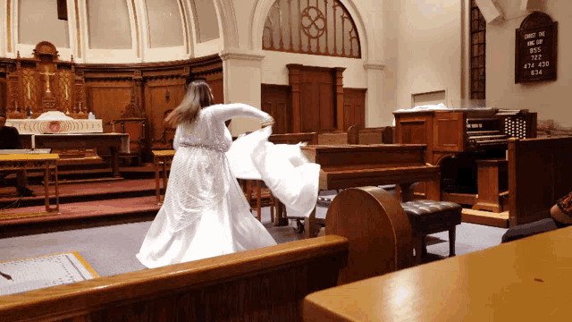 a woman in a white dress is dancing in a church with a sign on the wall that says jesus is love