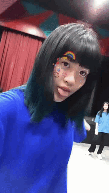 a girl wearing a blue shirt has a rainbow on her face