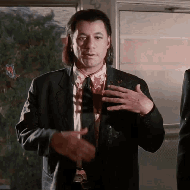 a man in a suit and tie with blood on his shirt is standing in front of a window .