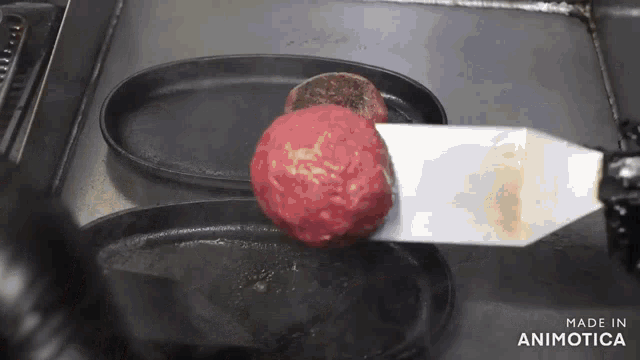 a spatula is being used to flip a hamburger patty on a pan that says made in animotica on the bottom