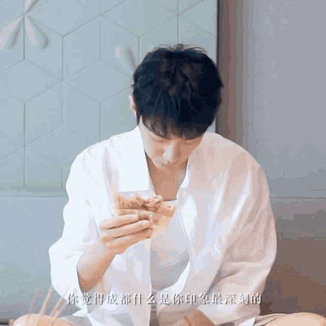 a man in a white shirt is sitting on the floor eating a piece of food