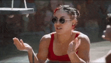 a woman in a red bikini and sunglasses is sitting on a swing in a pool .