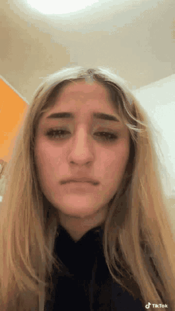 a young woman with long blonde hair is crying and making a sad face .