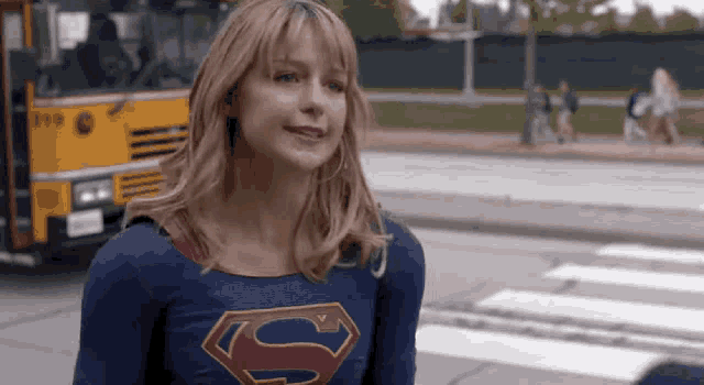 a woman in a superman costume is standing in front of a yellow school bus