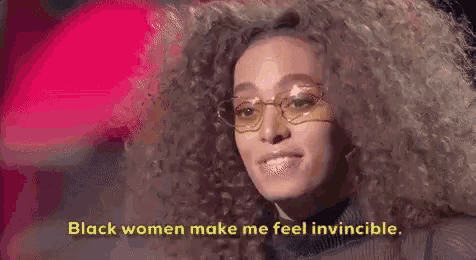 a woman with curly hair and glasses is smiling and says `` black women make me feel invincible . ''