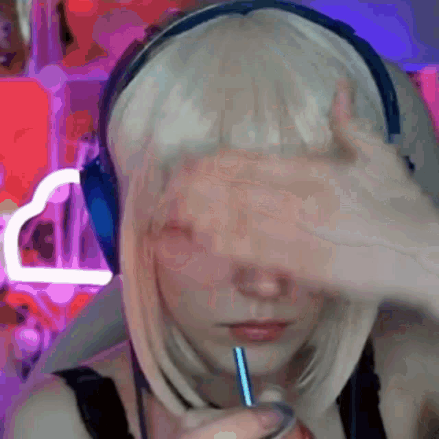 a woman wearing headphones and a blonde wig is covering her face with her hand .