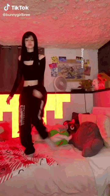 a girl in a black crop top and black pants is dancing on a bed .