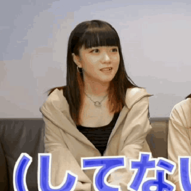 a girl is sitting on a couch with a necklace on her neck and a hoodie on .