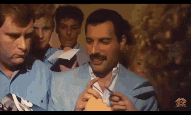 a group of men are standing around a man in a blue suit with a mustache
