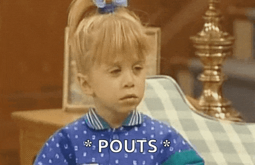 a little girl in a blue shirt is sitting on a couch and says pouts .