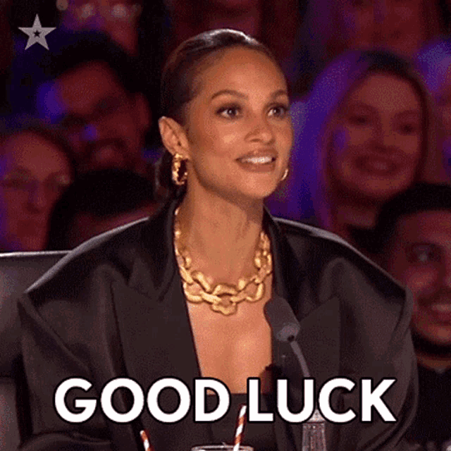 a woman in a black jacket is sitting in front of a microphone and says good luck .