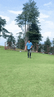 a man in a blue shirt and black jeans stands in a grassy field