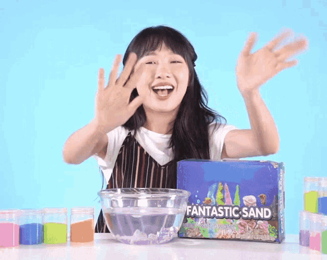 a box of fantastic sand sits on a table next to a girl