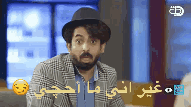 a man with a beard wearing a plaid jacket and a hat with arabic writing on it