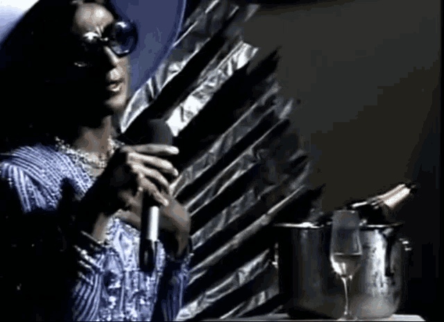a woman singing into a microphone next to a bottle of wine