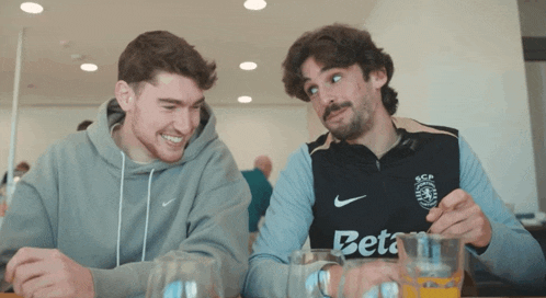 two men sitting at a table with one wearing a shirt that says beta on it