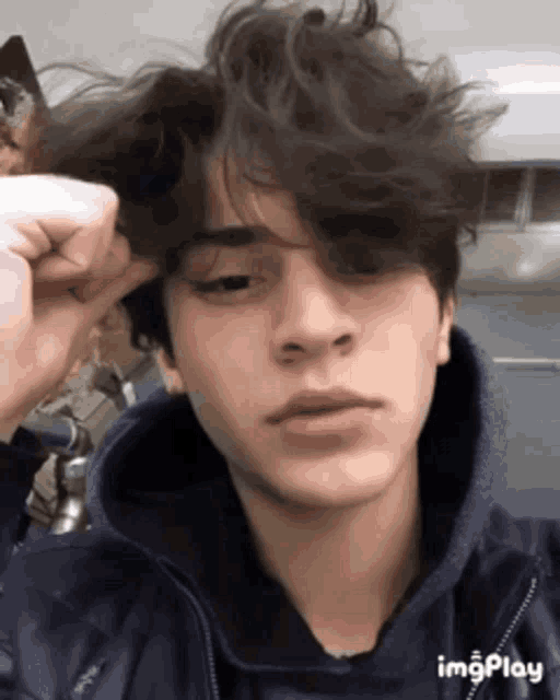 a young man in a blue jacket is taking a selfie with his hand in his hair .