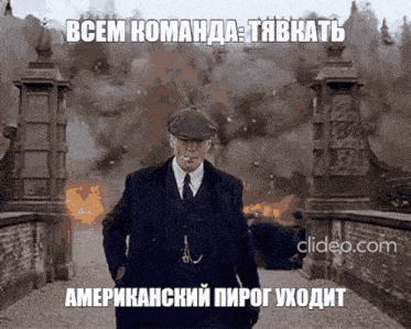 a man in a suit and tie is standing in front of a huge explosion and says " всем команда " in russian