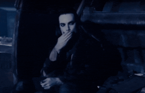 a man with long black hair is sitting in front of a sign that says " no smoking "