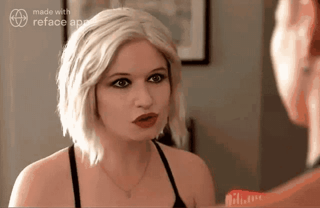 a woman with blonde hair and red lips looks at herself in the mirror .