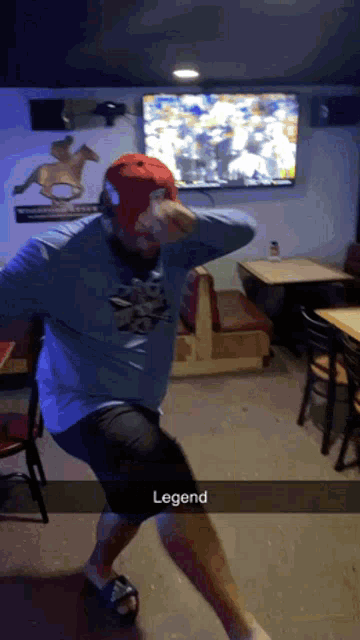 a man in a blue shirt and red hat is dancing in a room with the word legend on the bottom