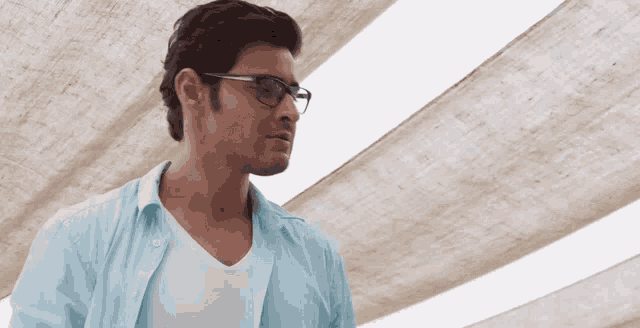 a man wearing glasses and a light blue shirt is looking down