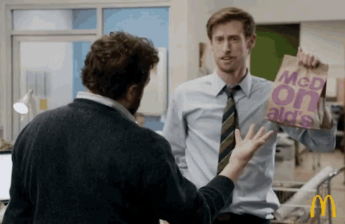 a man holding a bag that says mcdonald 's on it is talking to another man