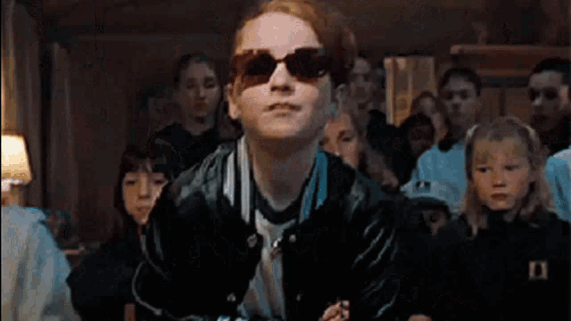 a group of young people wearing sunglasses are standing in a room .
