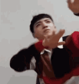 a man in a red and black sweater is making a funny face with his hands outstretched .