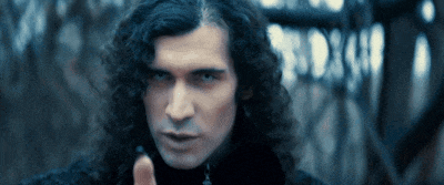 a man with long curly hair and a black turtleneck looks at the camera