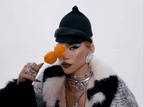 a woman wearing a black hat and a fur coat holds a piece of food in her hand