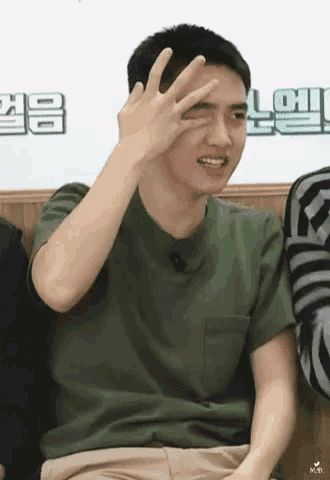 a man in a green shirt is making a peace sign with his hand