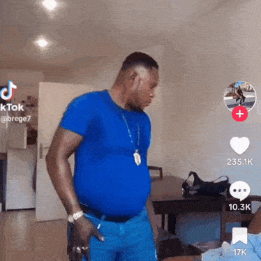 a man in a blue shirt is standing in a living room with a tiktok icon in the corner