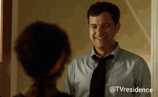 a man in a suit and tie is smiling while talking to a woman .