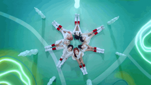 a group of girls are laying in a circle on a green surface