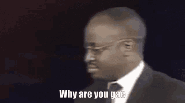 a man in a suit and tie is standing in front of a black background and saying `` why are you gae '' .