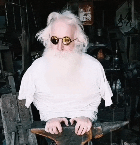 a man with a beard is sitting on an anvil with a sign behind him that says standing any time