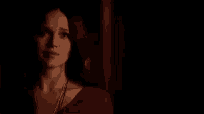 a woman in a red dress is standing in a dark room and looking at the camera .