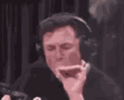 a man is smoking a cigarette with smoke coming out of his mouth while wearing headphones .