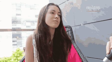 a woman is sitting in a chair with a remote control in her hand and looking at the camera .