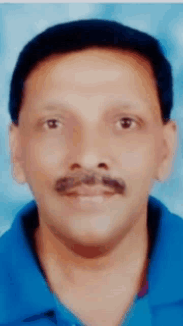 a man with a mustache wearing a blue shirt looks at the camera